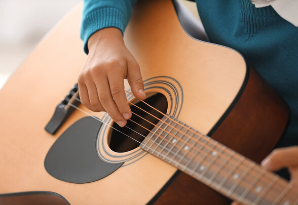 Gros plan sur les mains d'un jeune musicien pinçant les cordes d'une guitare acoustique - Agrandir l'image, fenêtre modale