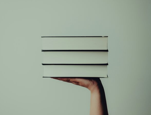 Une main soutenant en équilibre une pile de trois livres aux couvertures blanches sur fond neutre - Agrandir l'image, fenêtre modale