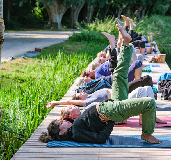 Séance collective de yoga sur un ponton en bois au bord d'une rivière, participants allongés jambes levées - Agrandir l'image, fenêtre modale