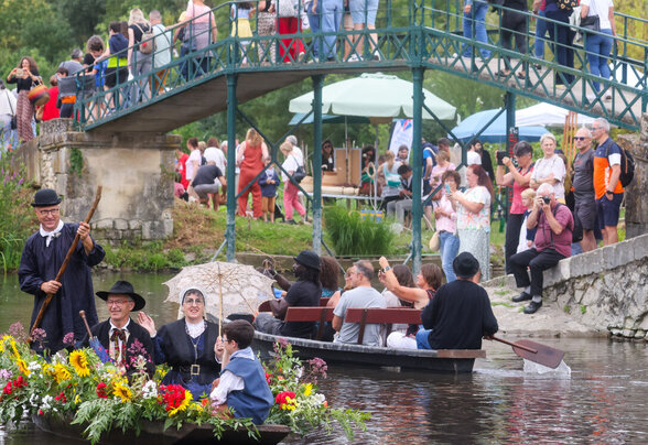 Barque fleurie avec participants en costume d'époque naviguant devant une foule nombreuse massée sur les berges et le pont - Agrandir l'image, fenêtre modale