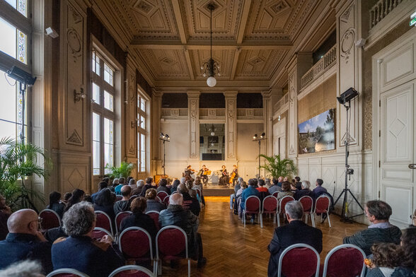 Ensemble de musique de chambre en concert dans une salle historique à décor ouvragé, face au public assis - Agrandir l'image, fenêtre modale