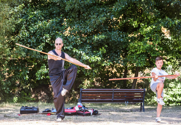 Un instructeur et un enfant pratiquent le kung fu avec des bâtons dans un parc - Agrandir l'image, fenêtre modale