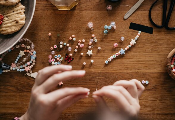 Mains d'une personne enfilant des perles colorées et des lettres sur un fil pour créer un bracelet - Agrandir l'image, fenêtre modale