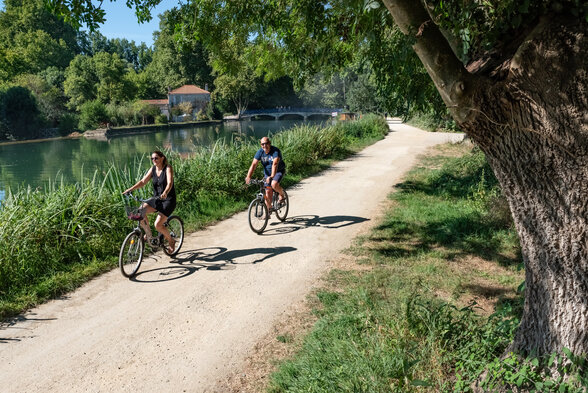 Deux cyclistes sur un chemin de halage ombragé longeant une rivière, végétation dense et pont en arrière-plan - Agrandir l'image, fenêtre modale