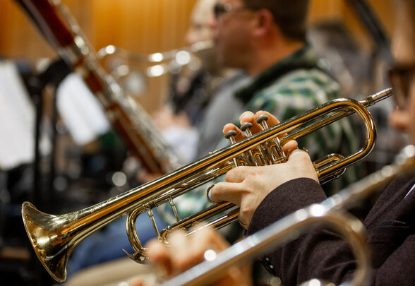 Gros plan sur une trompette dorée entre les mains d'un musicien, autres instrumentistes flous en arrière-plan - Agrandir l'image, fenêtre modale
