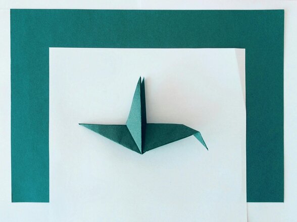 Grue en papier vert foncé (tsuru), figure symbolique façonnée à partir d'une simple feuille, posée sur fond blanc - Agrandir l'image, fenêtre modale