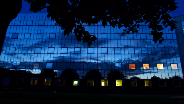 Façade en verre d'un bâtiment niortais de nuit, reflétant le ciel crépusculaire et les nuages, lumières intérieures allumées. - Agrandir l'image, fenêtre modale