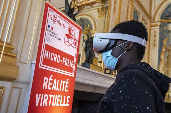 Un participant portant un casque de réalité virtuelle devant le panneau Micro-Folie du Ministère de la Culture - Agrandir l'image, fenêtre modale