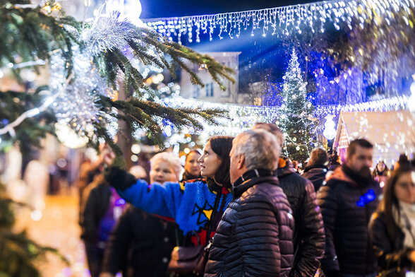Habitants découvrant les décorations de Noël en centre-ville, au pied d'un sapin orné de guirlandes lumineuses - Agrandir l'image, fenêtre modale