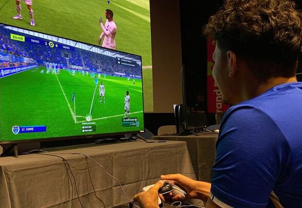 Un joueur tient une manette et joue à FIFA sur un grand écran lors du tournoi Level Up! - Agrandir l'image, fenêtre modale