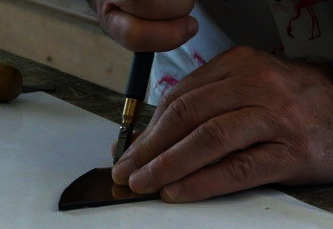 Mains tenant un coupe-verre pour entailler une pièce de verre coloré posée sur un plan de travail - Agrandir l'image, fenêtre modale