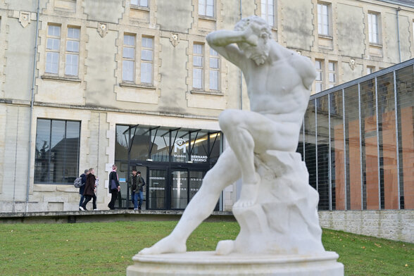 Statue en marbre blanc d'un homme en mouvement au premier plan devant l'entrée des Musées Bernard d'Agesci - Agrandir l'image, fenêtre modale