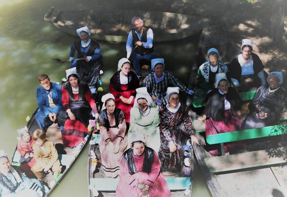 Participants en costumes traditionnels maraîchins à bord de barques sur un cours d'eau boisé - Agrandir l'image, fenêtre modale
